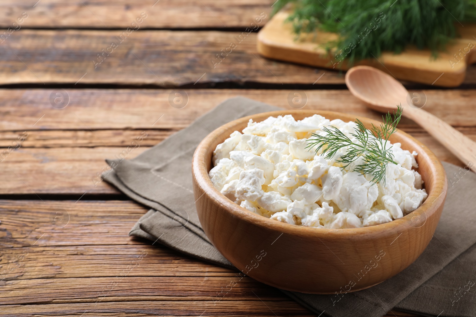 Photo of Fresh cottage cheese with dill in bowl on wooden table. Space for text