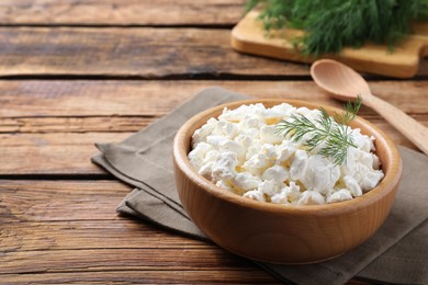 Photo of Fresh cottage cheese with dill in bowl on wooden table. Space for text
