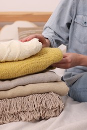 Photo of Woman with stack of different folded blankets and clothes on bed in room, closeup. Home textile