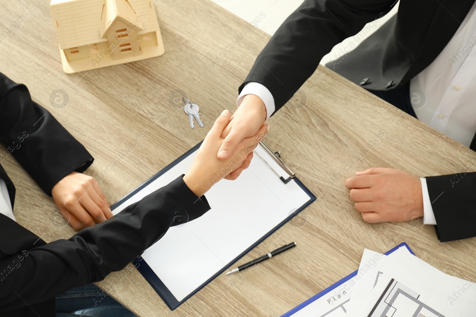 Photo of Real estate agent shaking hands with client at table in office, above view