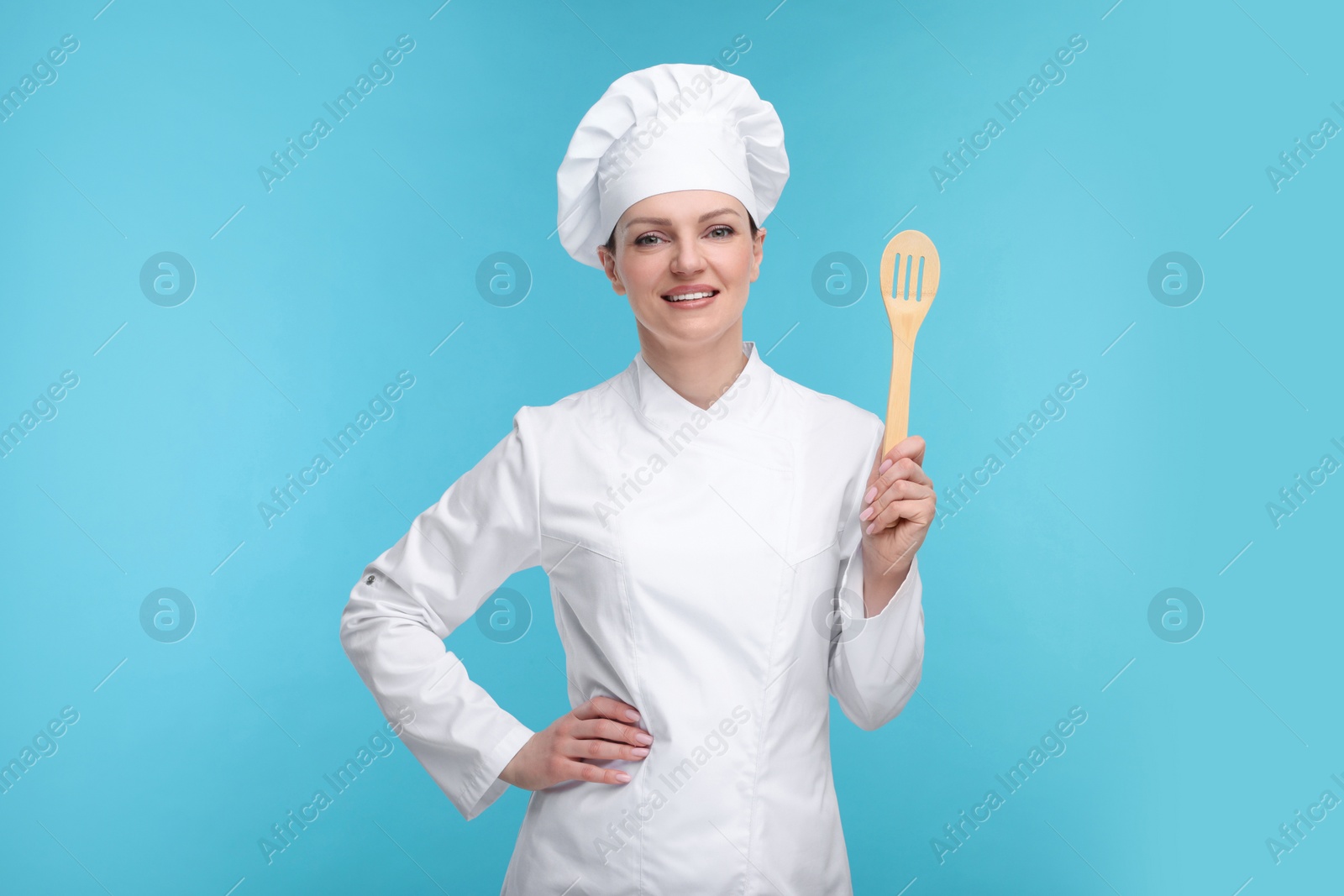 Photo of Happy chef in uniform holding wooden spatula on light blue background