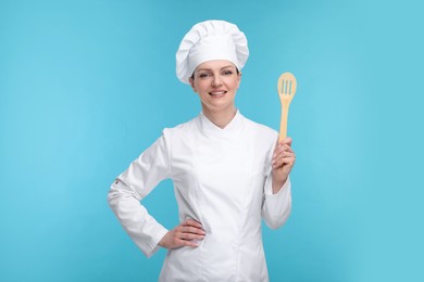 Happy chef in uniform holding wooden spatula on light blue background