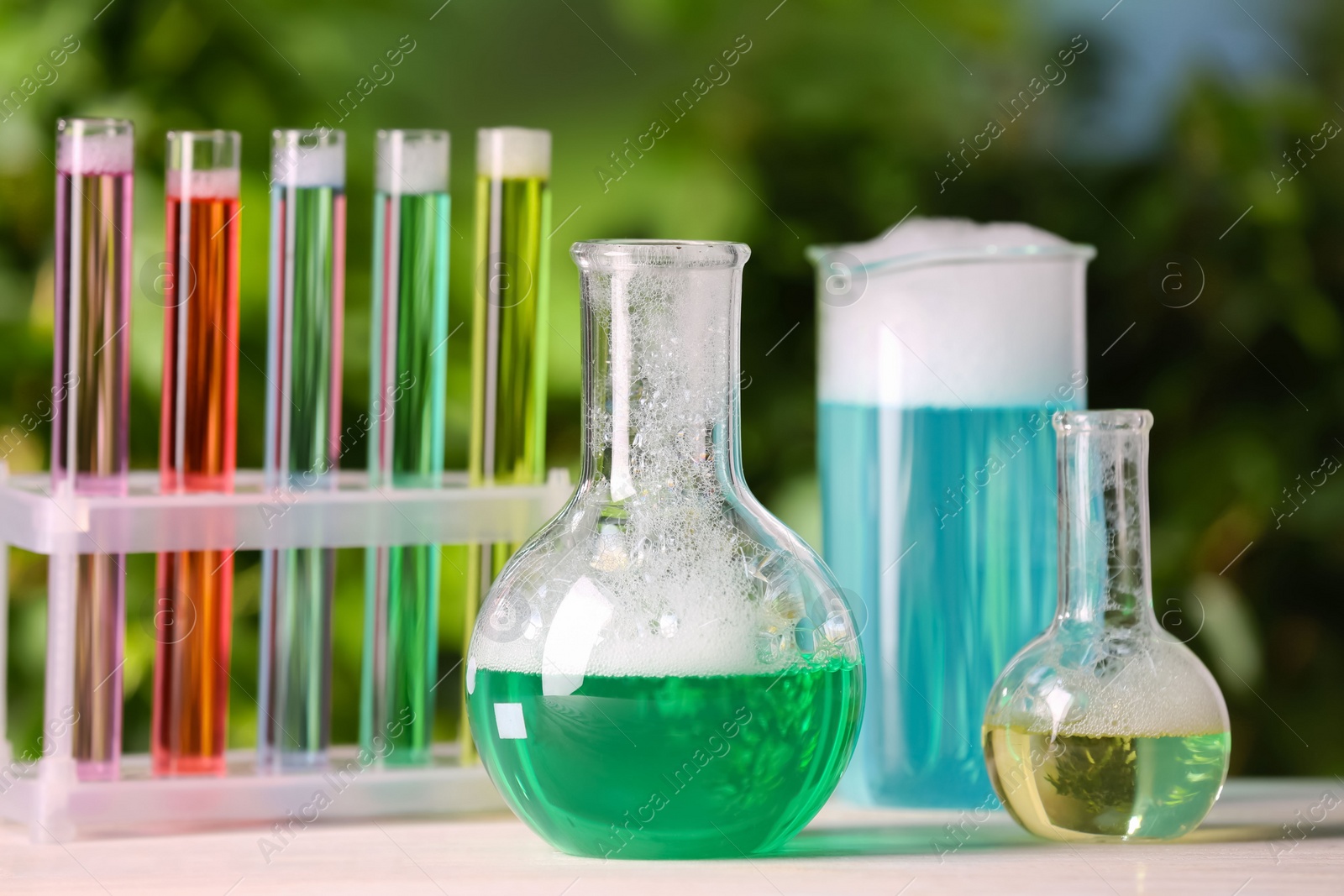 Photo of Laboratory glassware and test tubes with colorful liquids on white table outdoors. Chemical reaction