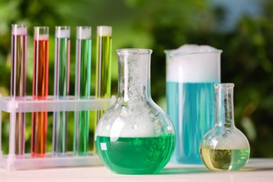 Laboratory glassware and test tubes with colorful liquids on white table outdoors. Chemical reaction