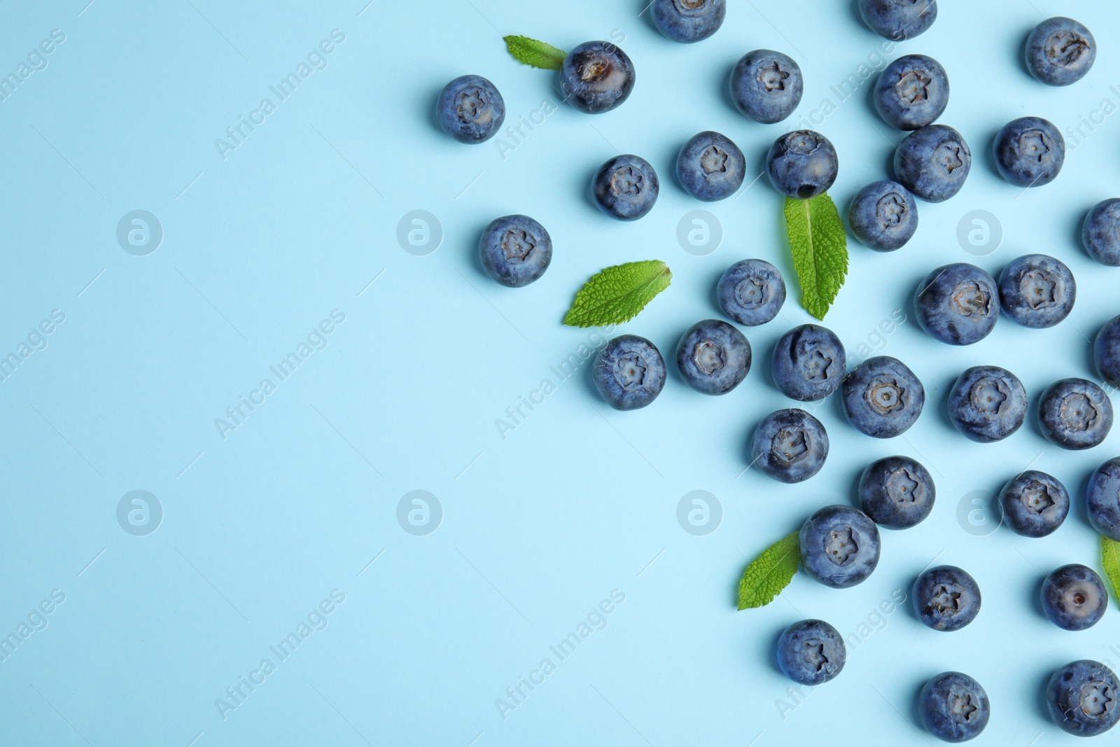 Photo of Tasty ripe blueberries and leaves on blue background, flat lay with space for text