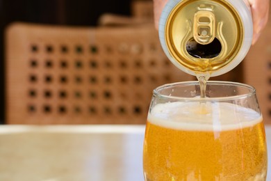 Photo of Man pouring beer from can into glass at table, closeup. Space for text