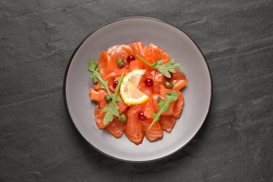 Photo of Salmon carpaccio with capers, cranberries, arugula and lemon on black table, top view