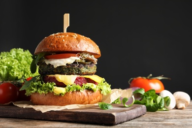 Photo of Vegan burger and vegetables on table against dark background. Space for text
