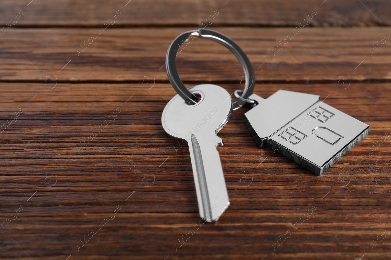 Photo of Key with keychain in shape of house on wooden table, closeup. Space for text