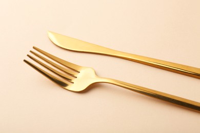 Photo of Stylish cutlery. Golden knife and fork on beige background, closeup