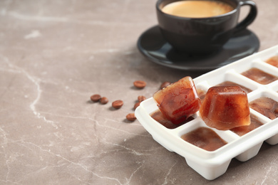 Photo of Ice cube tray with frozen coffee on grey table, closeup. Space for text