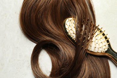 Photo of Stylish brush with brown hair strand on grey table, top view