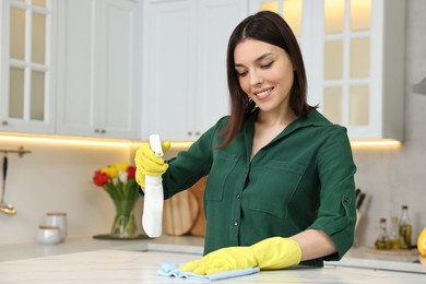 Photo of Woman cleaning table with rag and spray bottle in kitchen