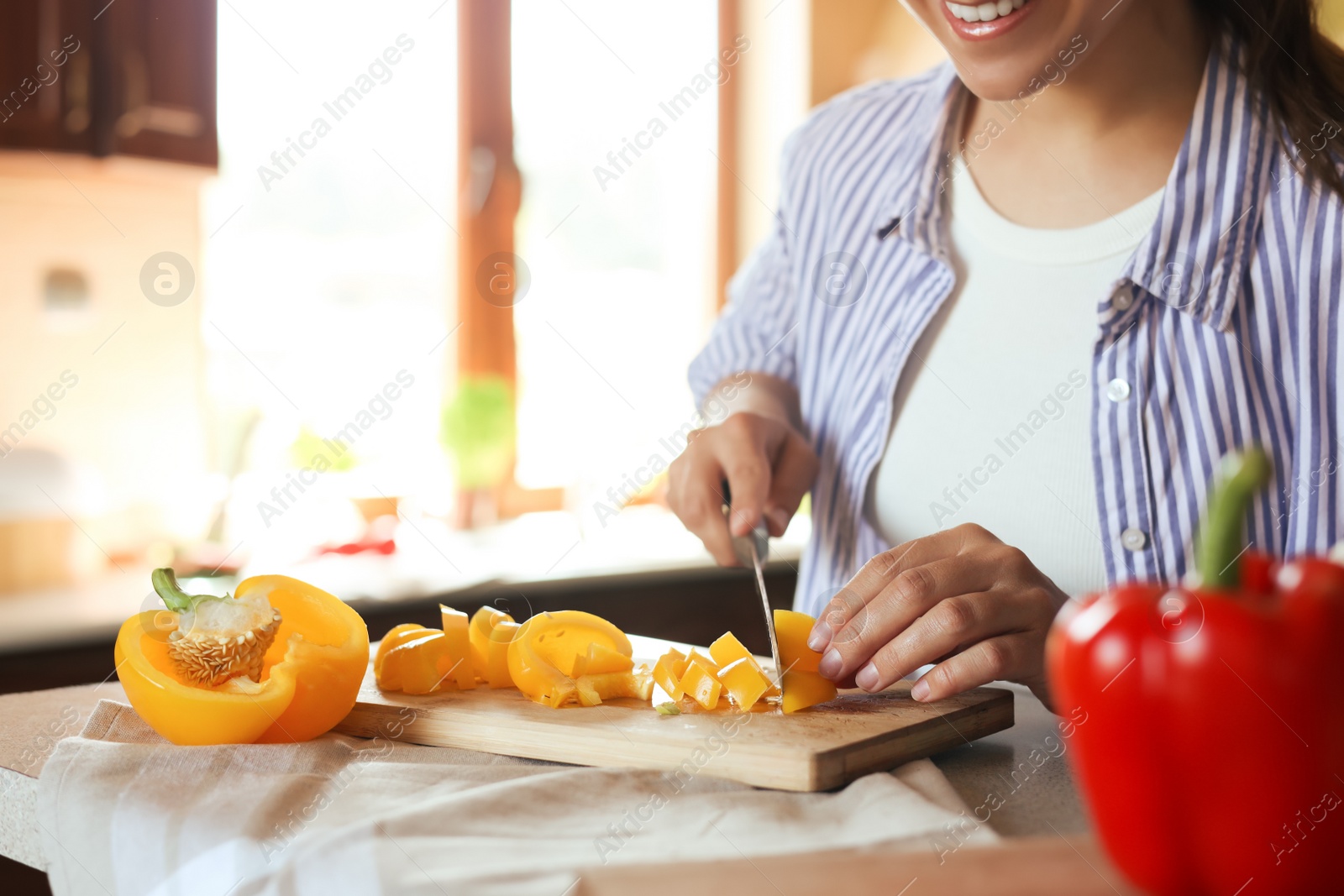 Photo of Woman cutting yellow bell peppers at countertop in kitchen, closeup. Space for text