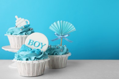 Baby shower cupcakes with toppers on white table against light blue background, space for text