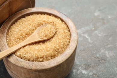 Brown sugar in bowl and spoon on grey textured table, closeup. Space for text