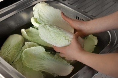 Photo of Woman washing fresh Chinese cabbages in sink, closeup