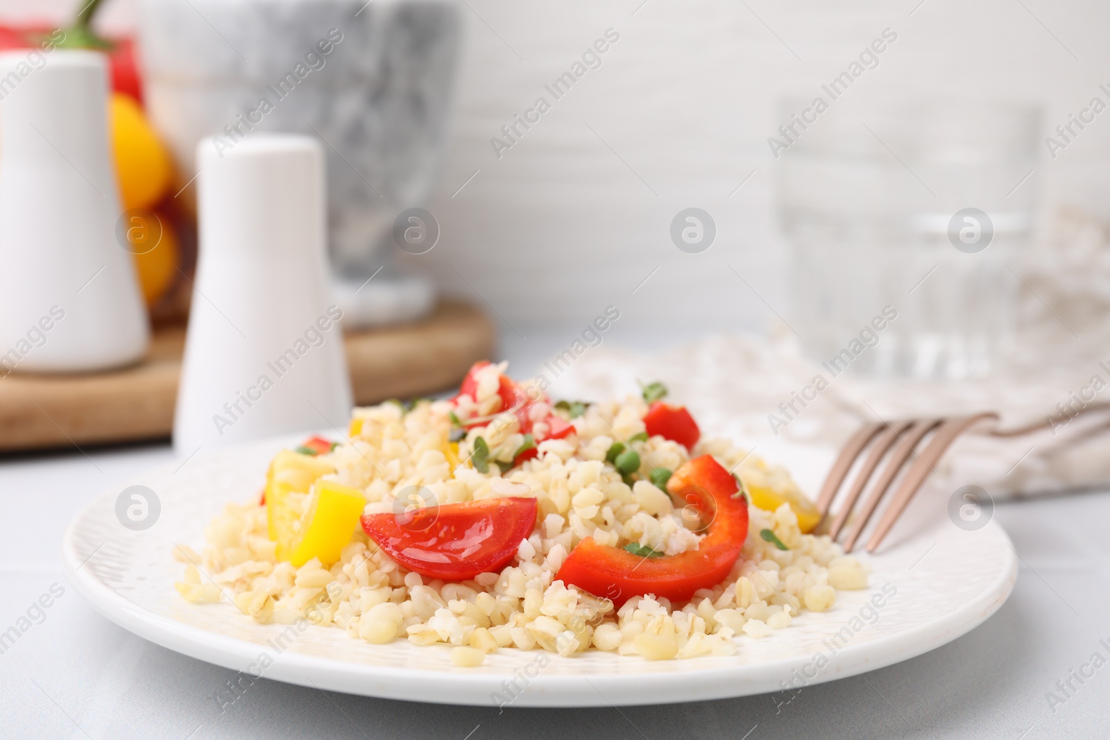 Photo of Plate of cooked bulgur with vegetables on white tiled table, closeup