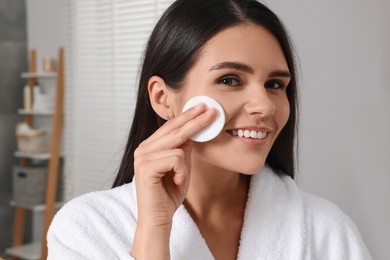 Young woman cleaning her face with cotton pad in bathroom