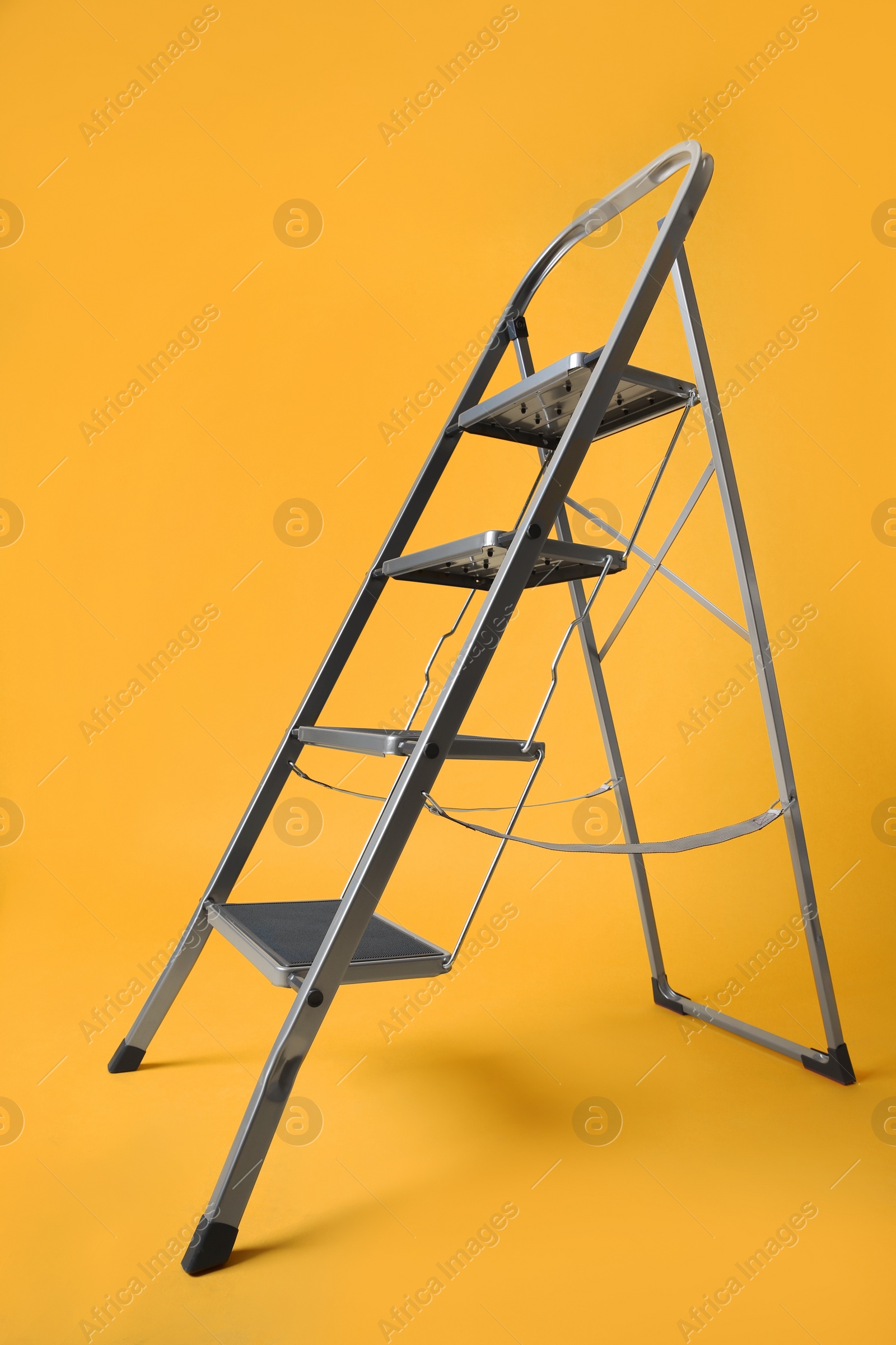 Photo of Modern metal stepladder on yellow background. Construction tool