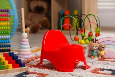 Photo of Red baby potty and toys on carpet in room. Toilet training
