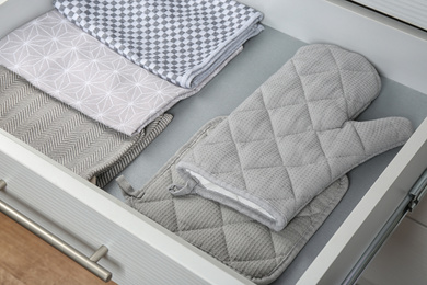 Photo of Open drawer with folded towels and oven mittens. Order in kitchen