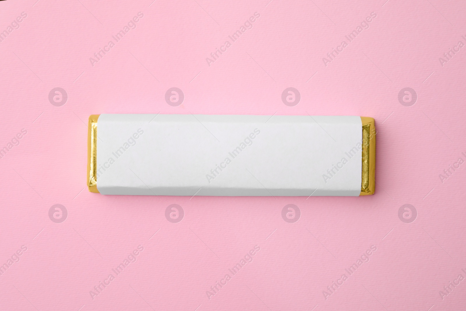 Photo of Tasty chocolate bar in package on pink background, top view