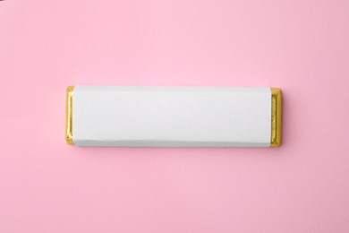 Photo of Tasty chocolate bar in package on pink background, top view