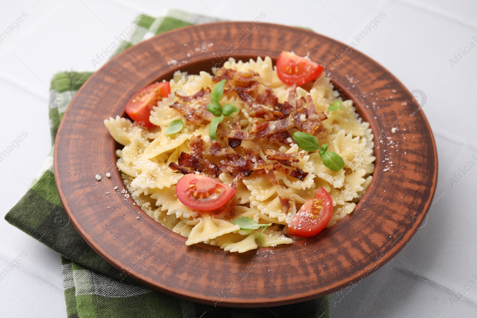 Photo of Tasty pasta with bacon, tomatoes and basil on white tiled table