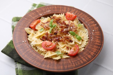 Tasty pasta with bacon, tomatoes and basil on white tiled table