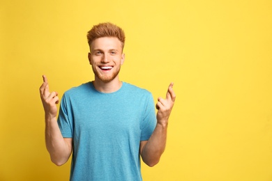 Photo of Portrait of happy young man with crossed fingers on yellow background