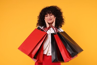 Happy young woman with shopping bags on yellow background