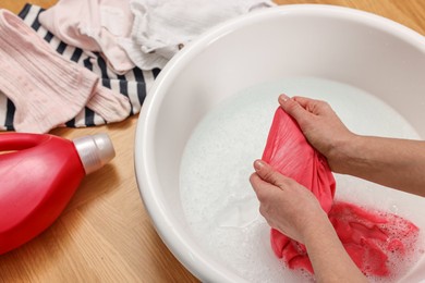 Woman washing baby clothes in basin on floor, closeup