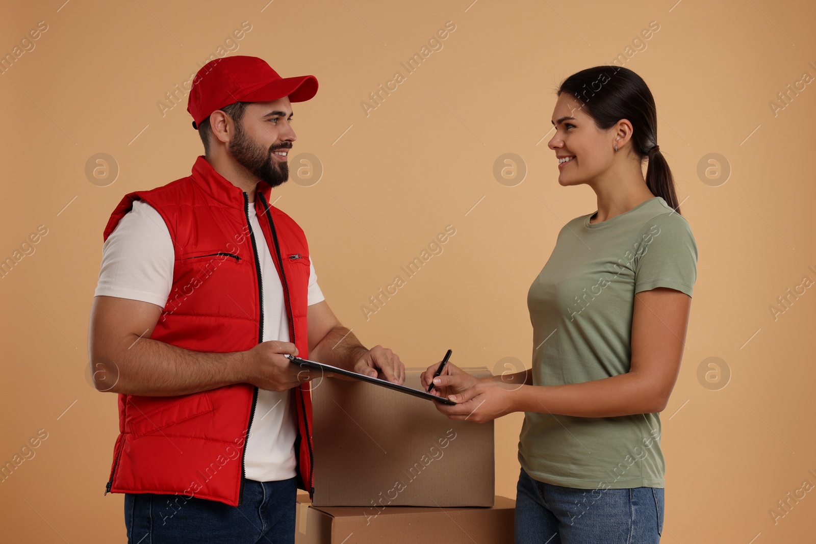 Photo of Smiling woman signing order receipt on light brown background. Courier delivery