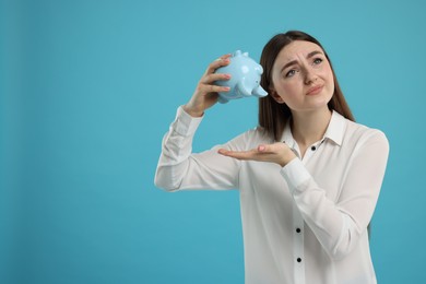 Sad woman with piggy bank on light blue background, space for text