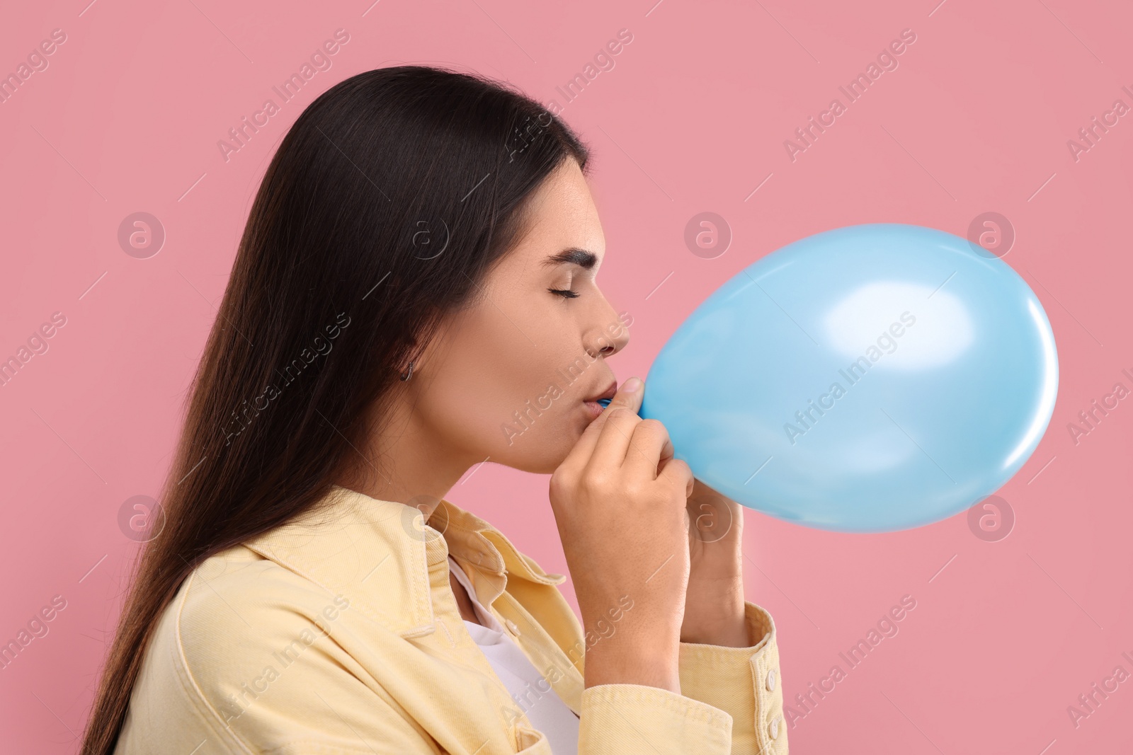 Photo of Woman inflating light blue balloon on pink background