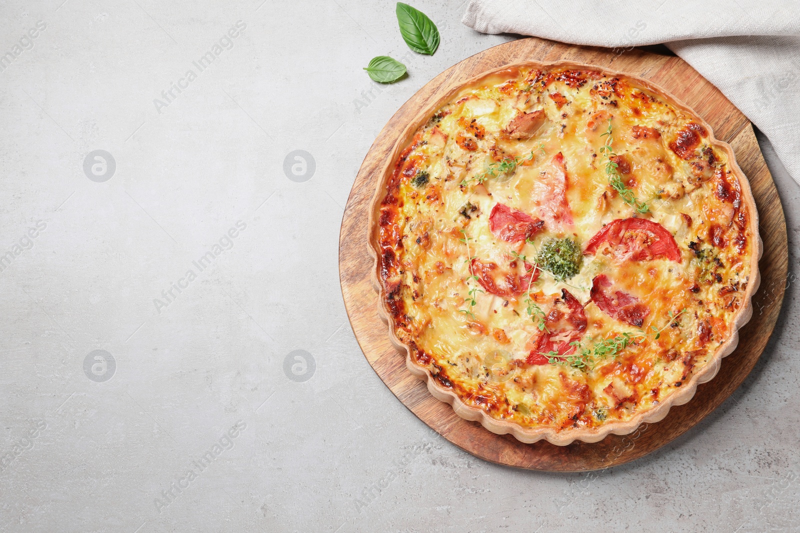 Photo of Tasty quiche with cheese, tomatoes and basil leaves on light grey table, flat lay. Space for text