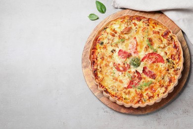 Photo of Tasty quiche with cheese, tomatoes and basil leaves on light grey table, flat lay. Space for text