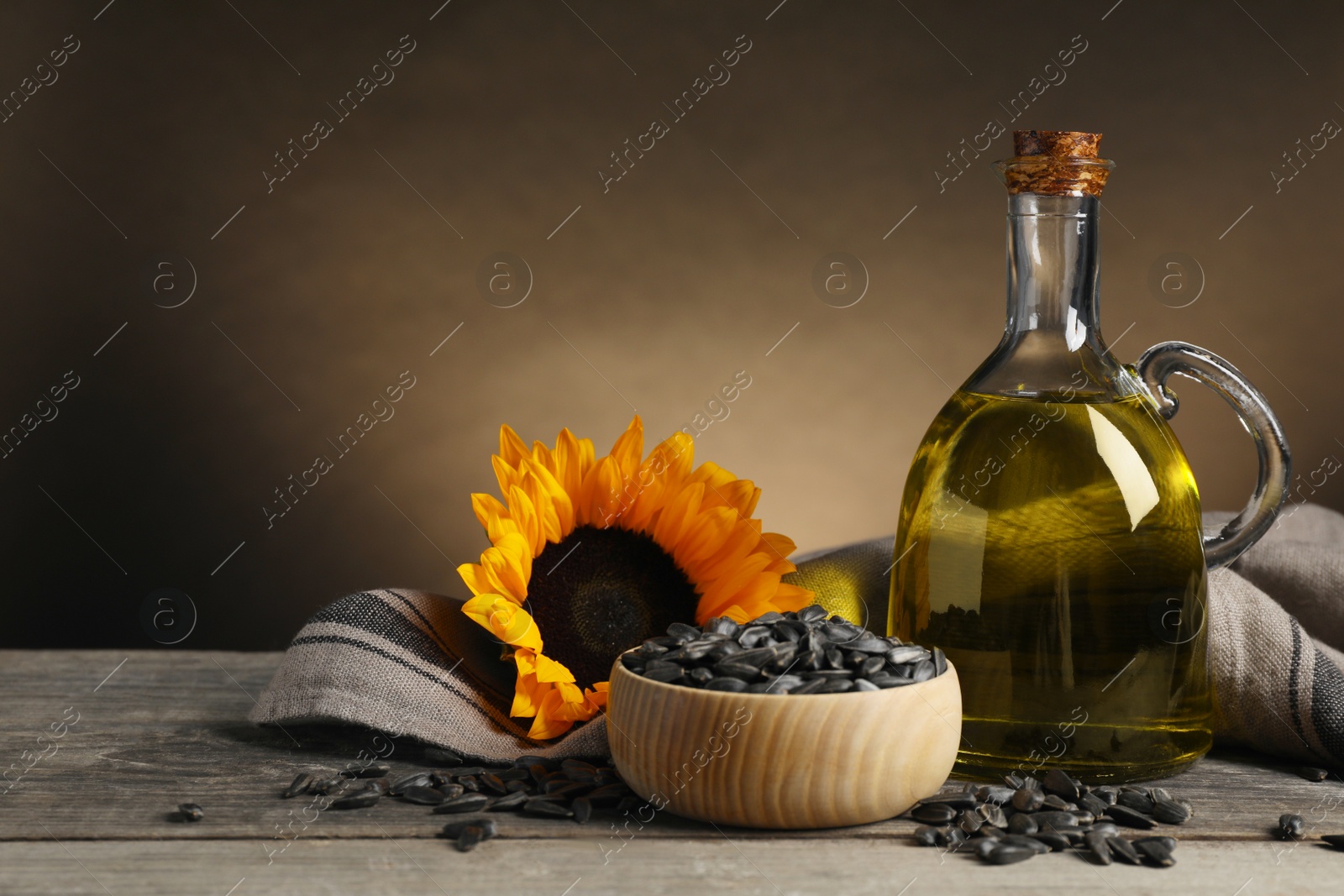 Photo of Sunflower cooking oil, seeds and yellow flower on light grey table, space for text