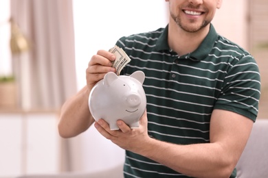 Man with piggy bank and money at home