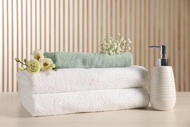 Photo of Soft folded towels, dispenser, gypsophila and eustoma flowers on light wooden table