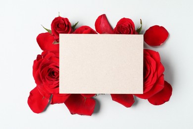 Blank card, beautiful red roses and petals on light background, top view. Space for text