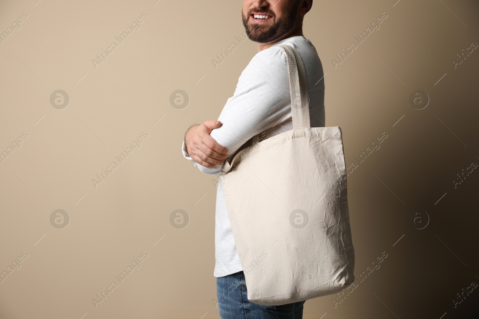 Photo of Happy young man with eco bag on beige background, closeup