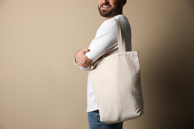 Happy young man with eco bag on beige background, closeup