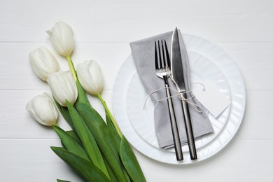 Photo of Stylish table setting with cutlery, blank card and tulips on white wooden background, flat lay
