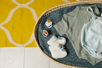 Photo of Basket with baby clothes and accessories on floor, top view. Space for text