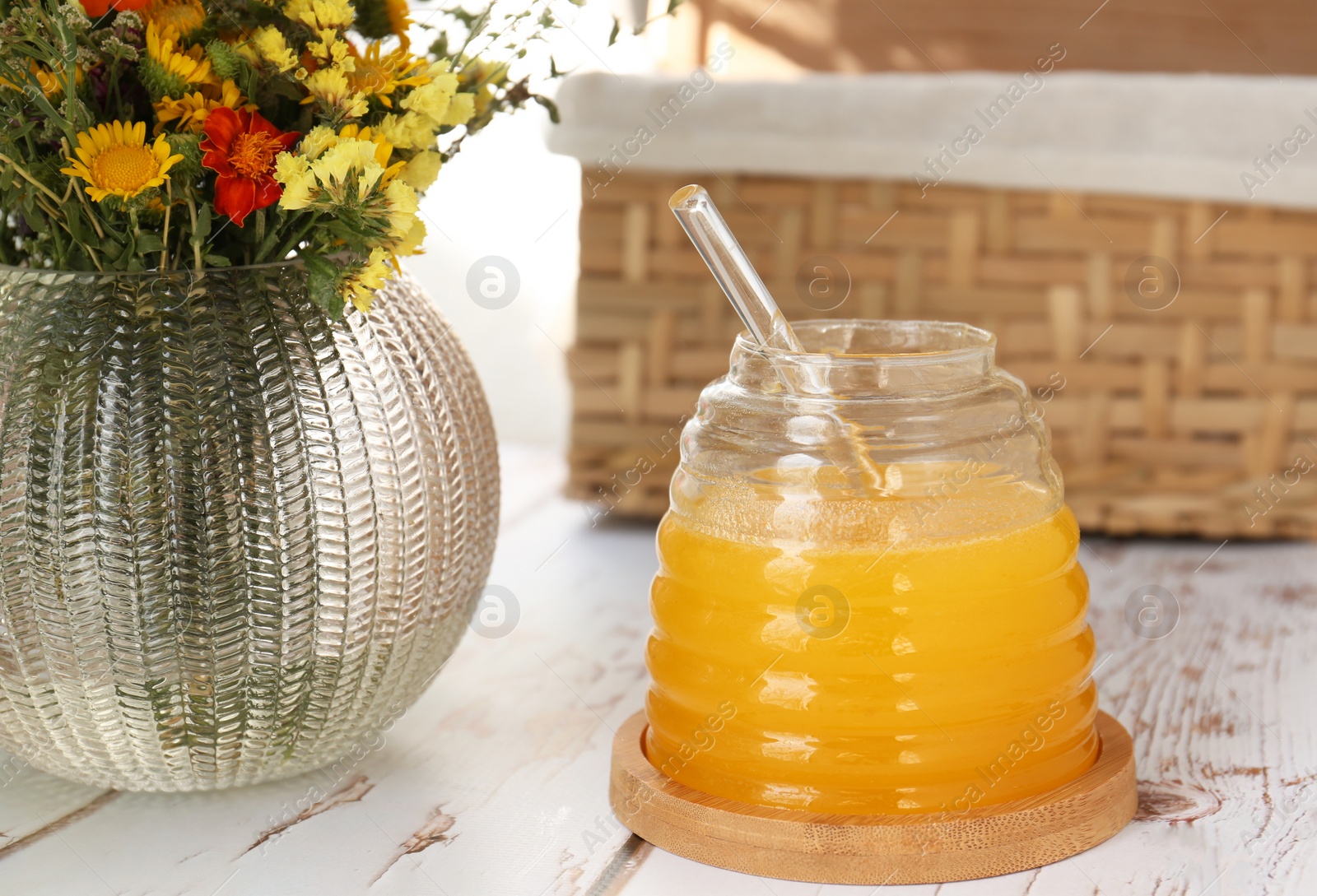 Photo of Delicious fresh honey and beautiful flowers on white wooden table indoors