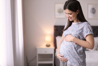 Young pregnant woman near window at home