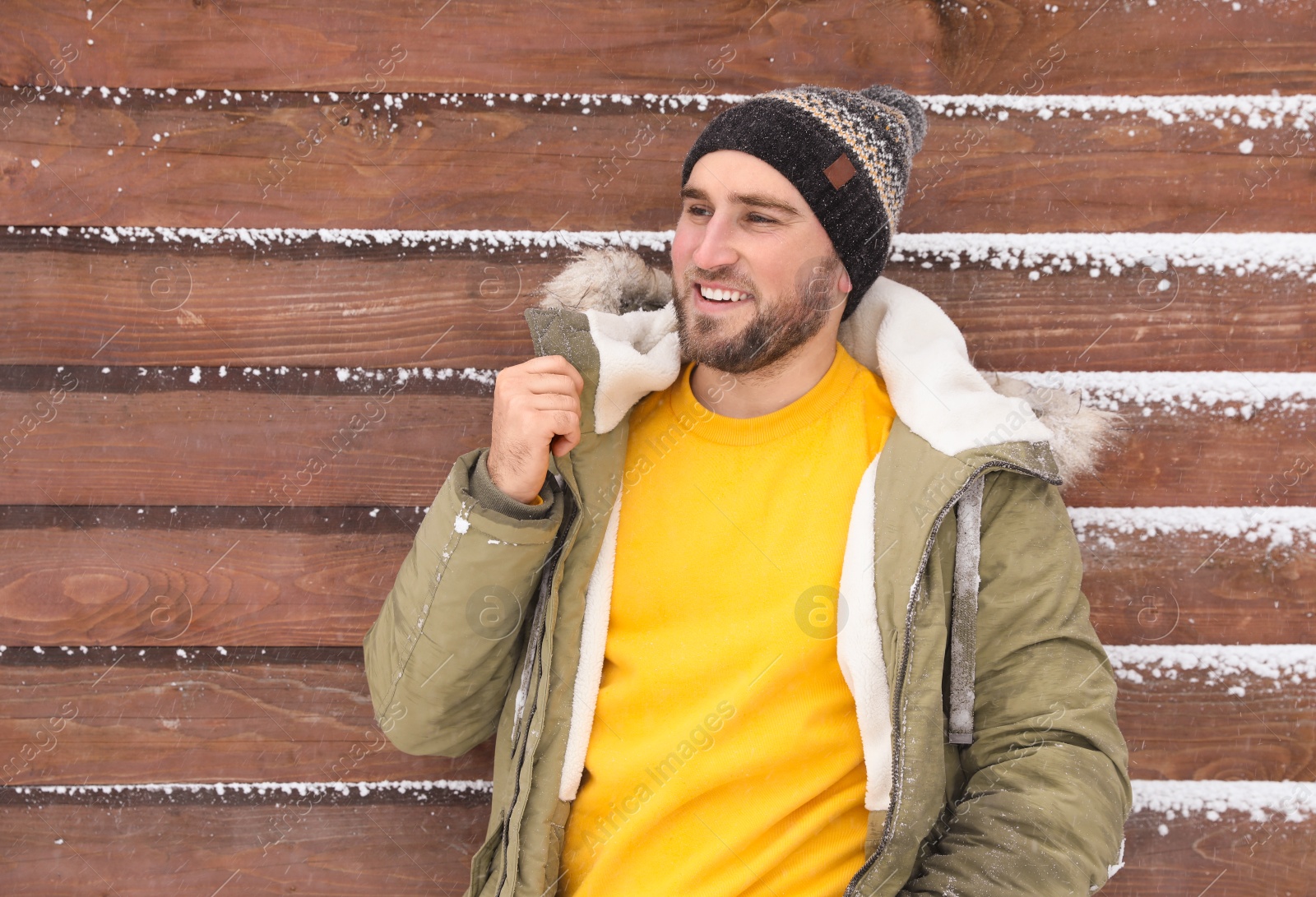 Photo of Young man wearing warm clothes near wooden wall.  Winter vacation