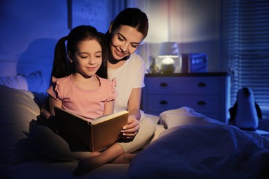 Photo of Mother with little daughter reading fairy tale in dark bedroom